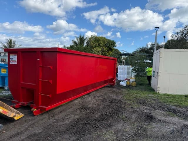 A large red roll-off dumpster on a job site, showing the scale of a full-size rental